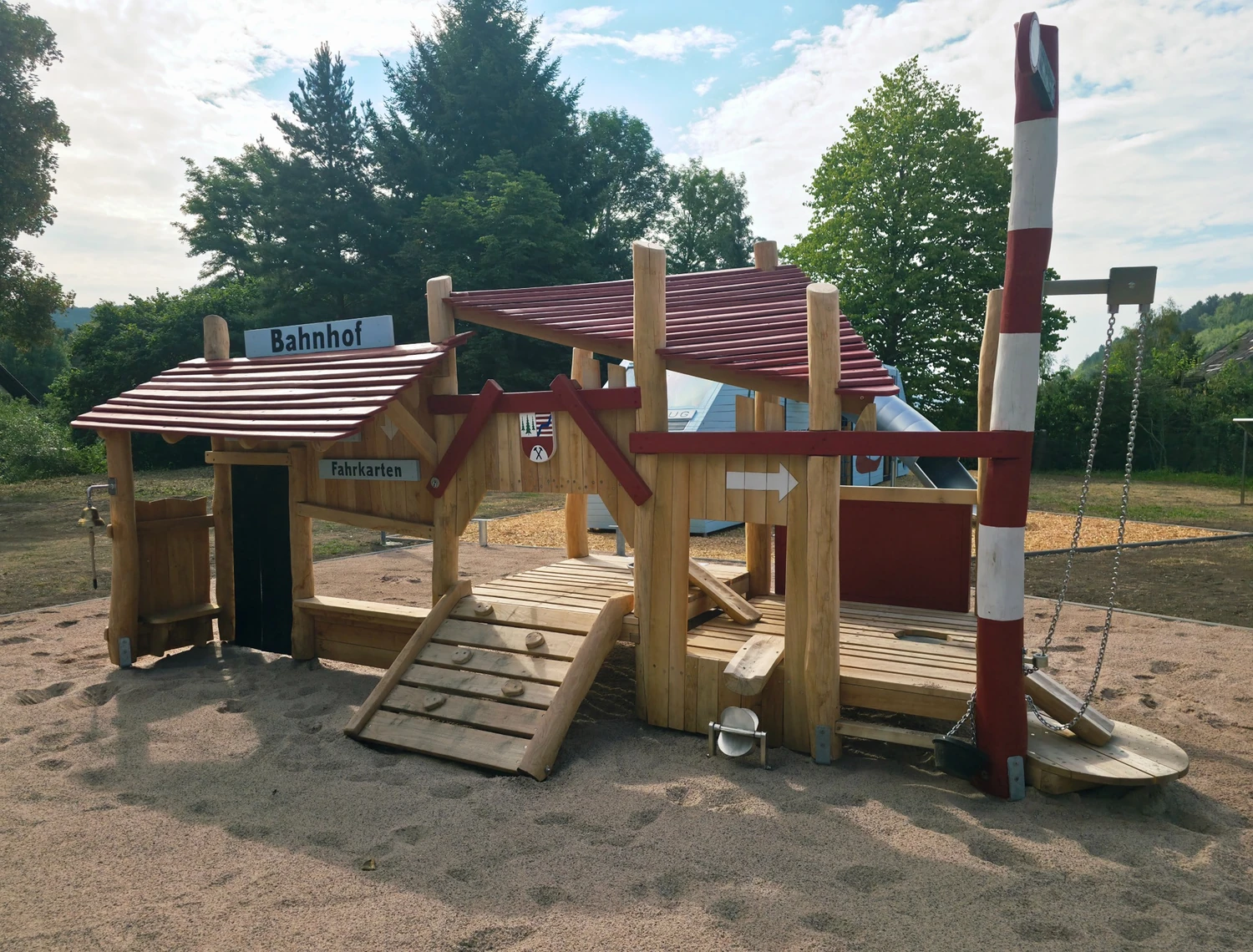 Hölzerner Spielplatz im Bahnhofsstil mit Kletterelementen, Rutsche und Schranke.