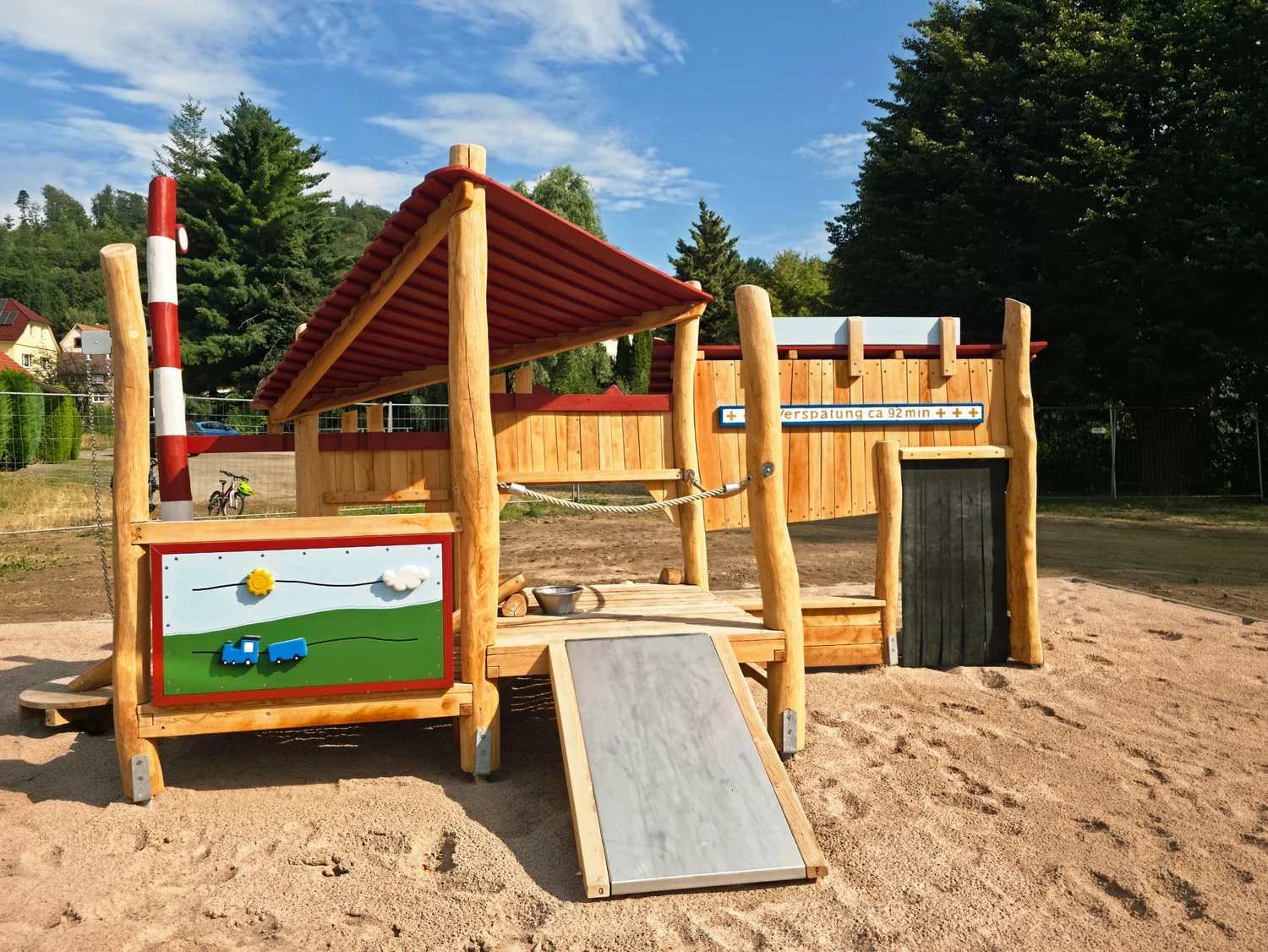 Hölzerne Spielanlage auf einem Abenteuerspielplatz mit Sandbereich, Spielstationen und Kletterelementen.