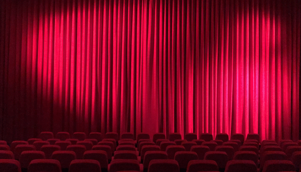 Theatersaal mit rotem Vorhang und roten Stühlen als Symbolbild für eine Theatervorstellung.