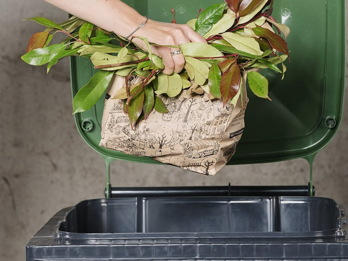 Person wirft Gartenabfälle in Papierverpackung in eine grüne Biotonne