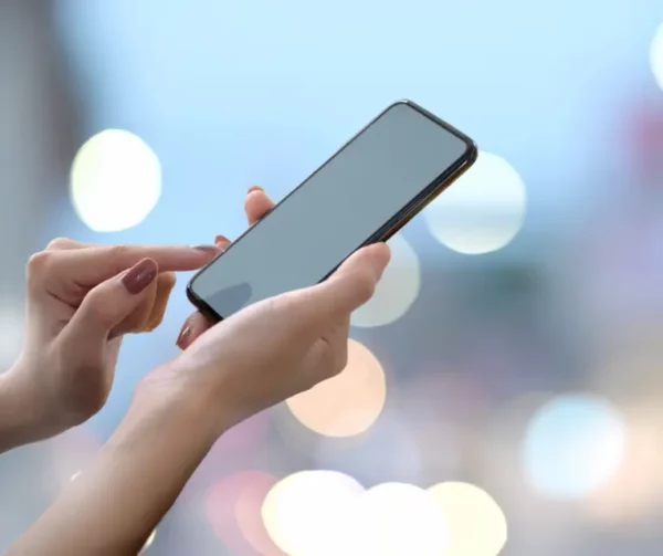 Frau hält Smartphone in der Hand und tippt auf den Bildschirm, unscharfer Hintergrund mit Lichtern