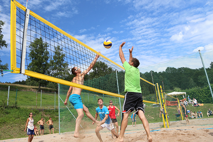 mehrere Personen spielen auf einem Sandplatz Beachvolleyball