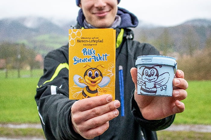 Bienenlehrpfad in Floh-Seligenthal, Eine Person hält einen Flyer und einen Becher mit einer gezeichneten Biene