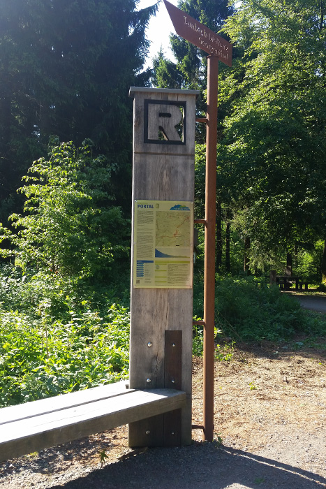 Wegweiser mit Schautafel und Bank vom Rennsteig, im Hintergrund Wald