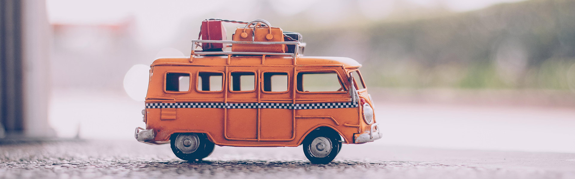 Ein orangener alter Spielzeug Minibus der mit Koffern auf dem Dach beladen ist.