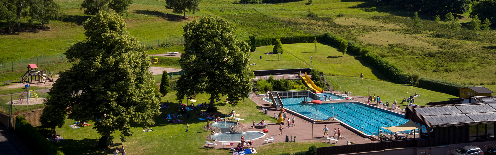 Bildausschnitt: Blick ins Schwimmbad, Rutsche und Schwimmbecken mit Besuchern