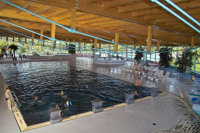 Gezeigt sind mehrere Wasserbecken (Poul mit Startblöcken, Wirlpool u.a.) Liegestühle