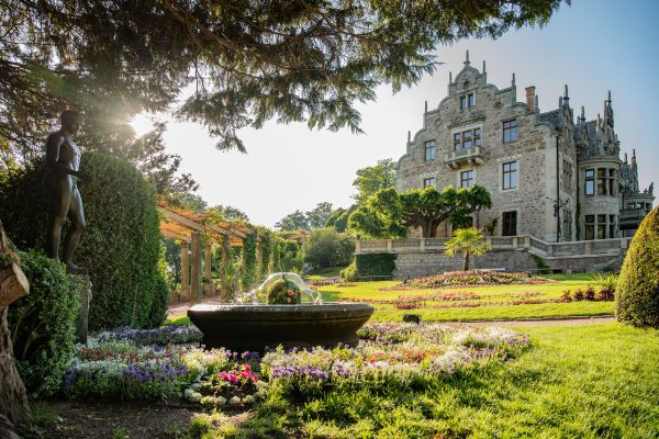 Schloss Altenstein in Bad Liebenstein mit historischem Garten, Idolinobrunnen, Blumenbeeten und Statue bei Sonnenschein.