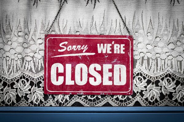 Rotes Schild mit der Aufschrift Sorry we're closed vor Spitzenvorhang