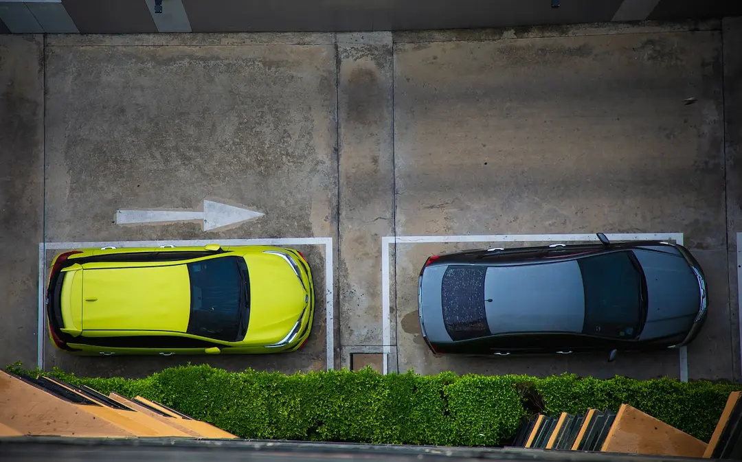 Zwei Autos in markierten Parkplätzen von oben fotografiert, gelbes Auto links, graues Auto rechts